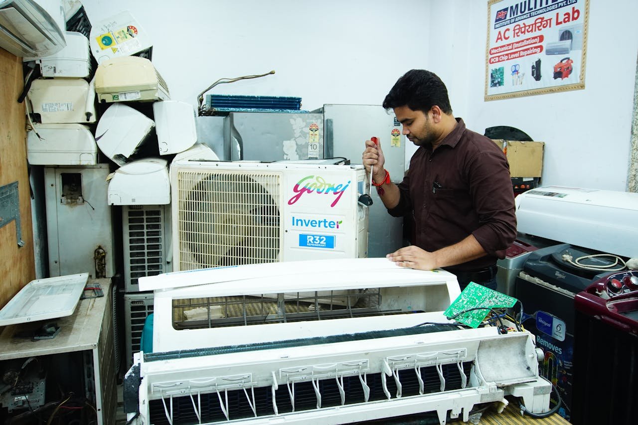 Technician repairing an air conditioner unit in New Delhi workshop.